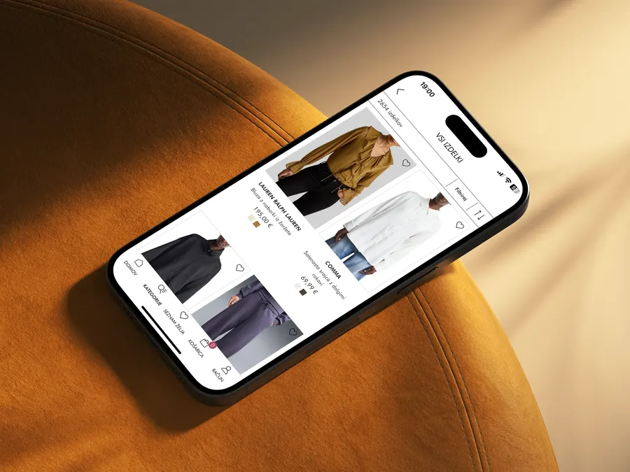 The Emporium app on a phone resting on an ochre velvet chair: a product grid with brands and prices
